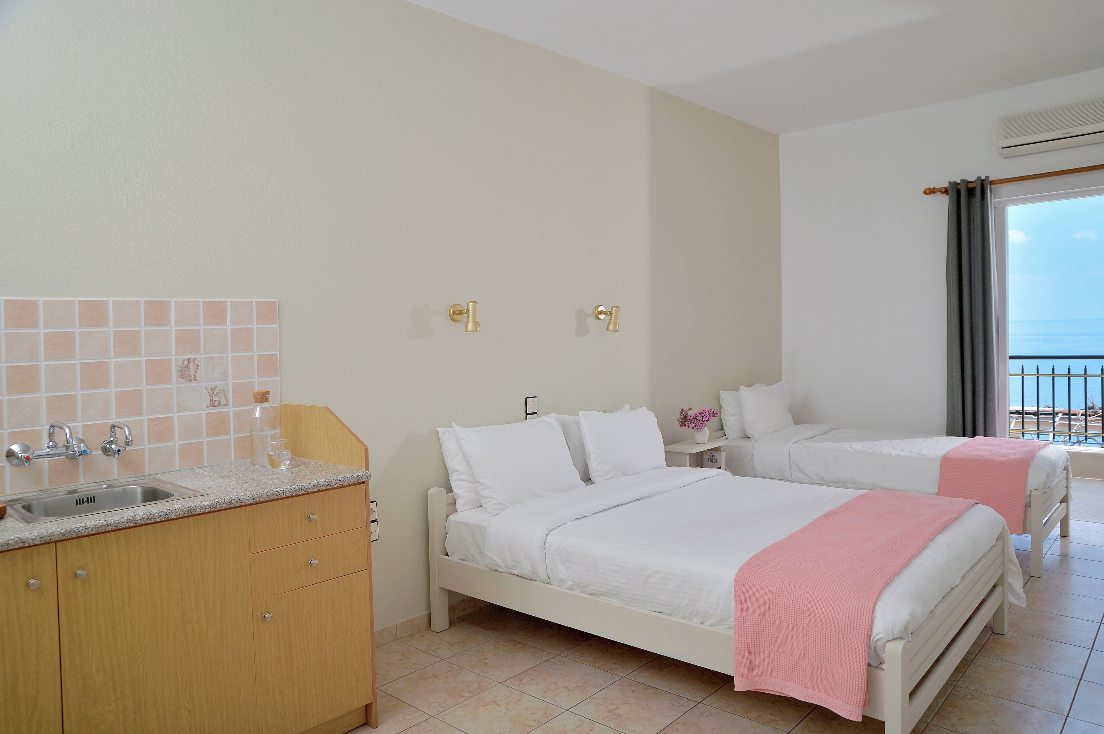 A hotel room with two beds, a sink, and a view of the sea.