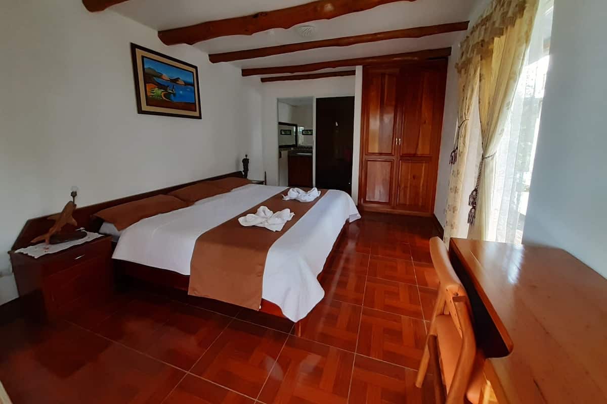A hotel room with a large bed, wooden beams on the ceiling, a wooden desk, and a wardrobe.