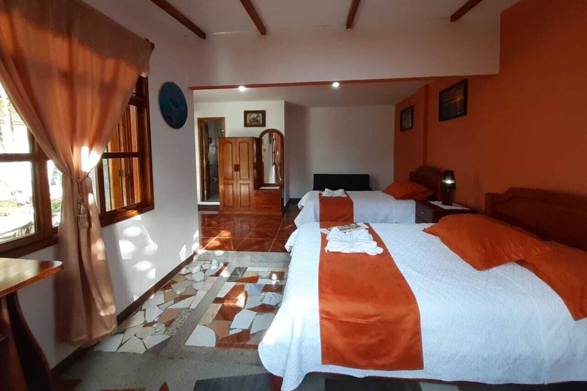 A hotel room with two beds, a wooden wardrobe, a bathroom with a mirror, and a tiled floor.