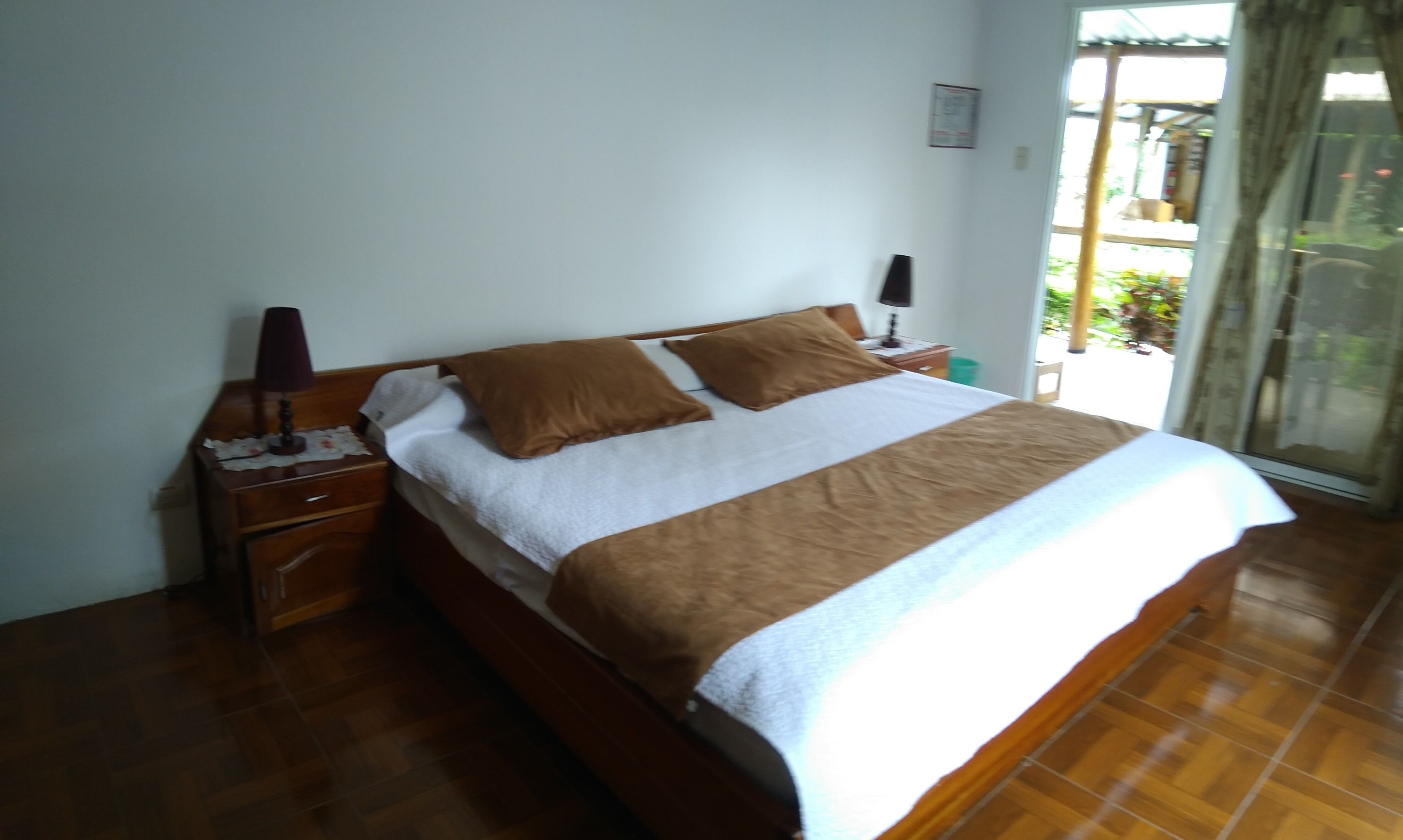 Un dormitorio con una cama de madera, una mesita de noche, una lámpara y una ventana con cortinas.