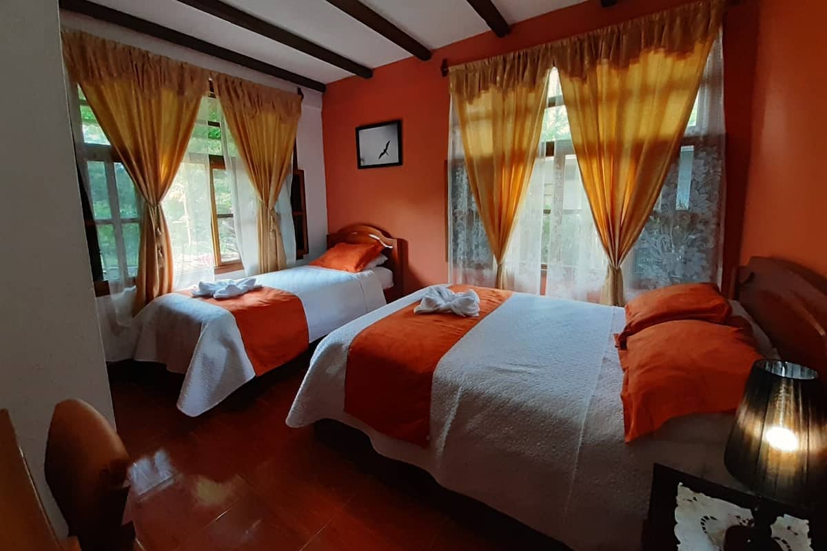 A room with two beds, each with an orange blanket, wooden headboards, and a window with curtains.