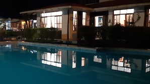 Vista nocturna de una piscina con edificios circundantes.