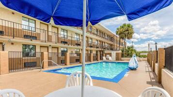 A hotel pool area with a blue canopy, a pool table, and white chairs.