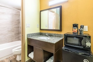 A bathroom with a granite countertop sink, a mirror, a microwave, and a coffee machine.