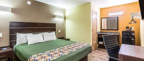 A hotel room with a bed, a desk, a chair, a microwave, and a small kitchenette.
