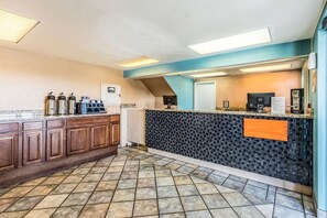 Une cuisine avec un mur recouvert de carreaux, des meubles en bois, un coin café et un comptoir équipé d’un ordinateur et d’un téléphone.