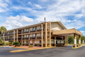 Un motel à plusieurs étages, doté de balcons, d’un parking couvert et offrant une vue sur un ciel dégagé.