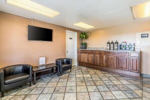 A reception area with a flat-screen TV, a reception desk, two leather chairs, a potted plant, a kitchen counter with appliances, and a tiled floor. - Tampa Inn Fairgrounds (Tampa)