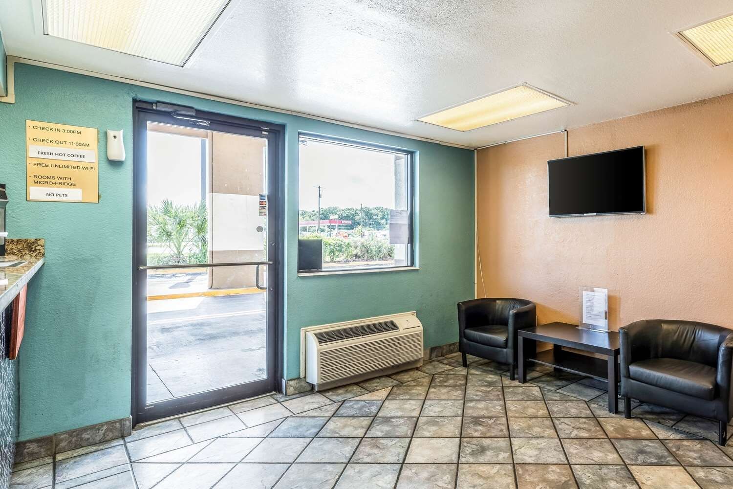 A room with a door, a window, a flat-screen TV, and a seating area with chairs.