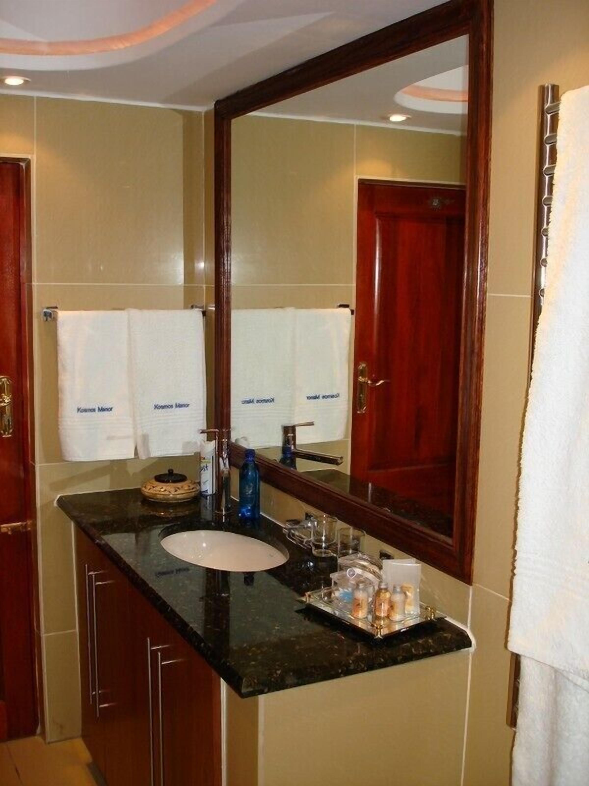 Un baño con lavamanos, espejo y dos toallas colgadas en la pared.