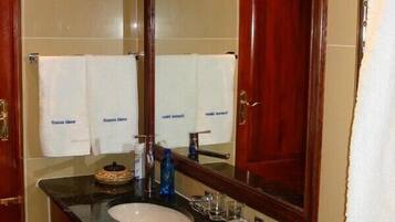 Un baño con lavamanos, espejo y dos toallas colgadas en la pared.