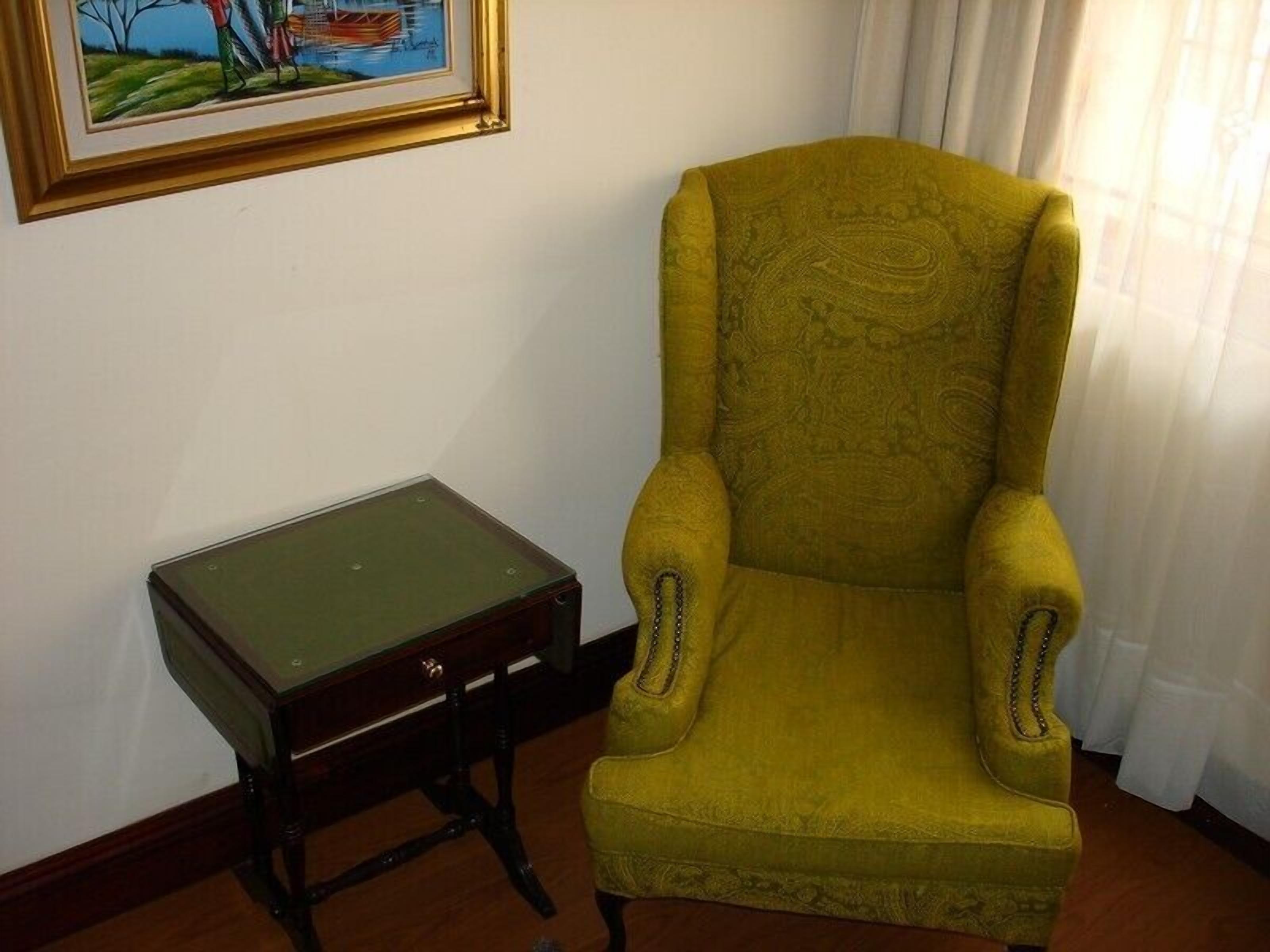 Una habitación con un sillón amarillo, una mesita de madera y un cuadro enmarcado en la pared.