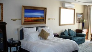 A hotel room with a large bed, a sofa, and a painting on the wall. - Kosmos Manor (Hartbeespoort)