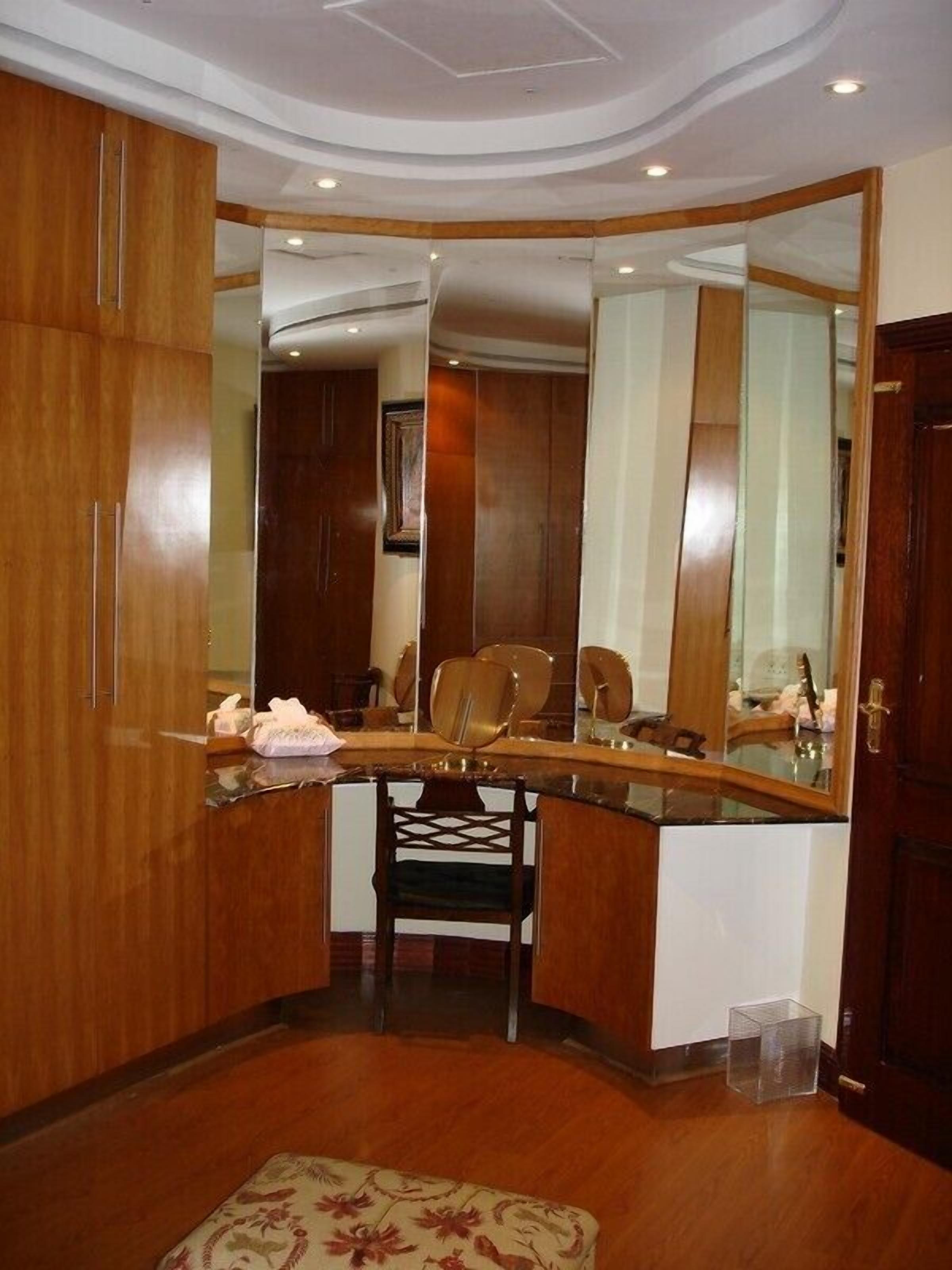 A room with a wooden vanity, a chair, a mirror, and a small rug.