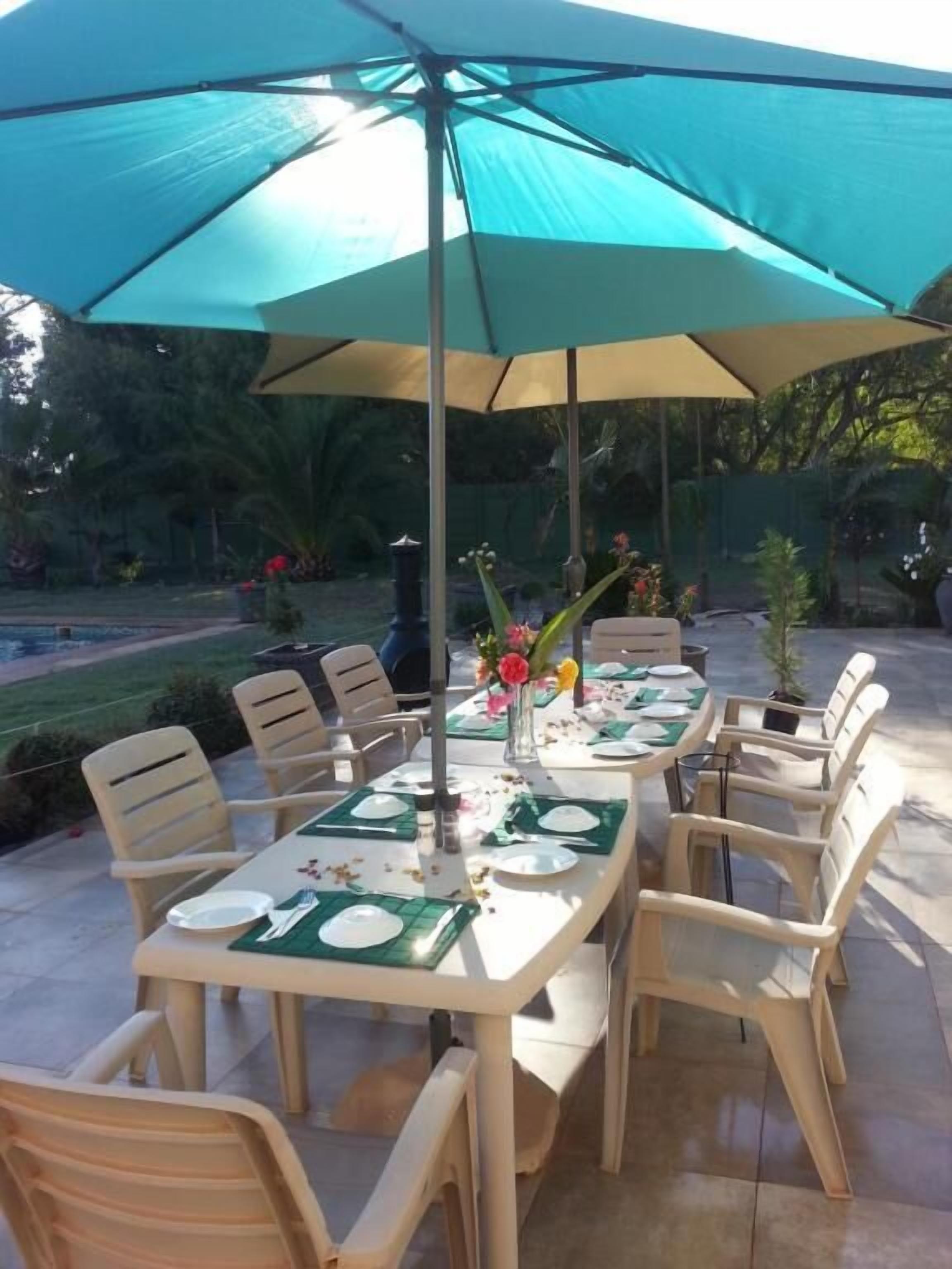 An outdoor patio with tables and chairs, covered by a large umbrella.