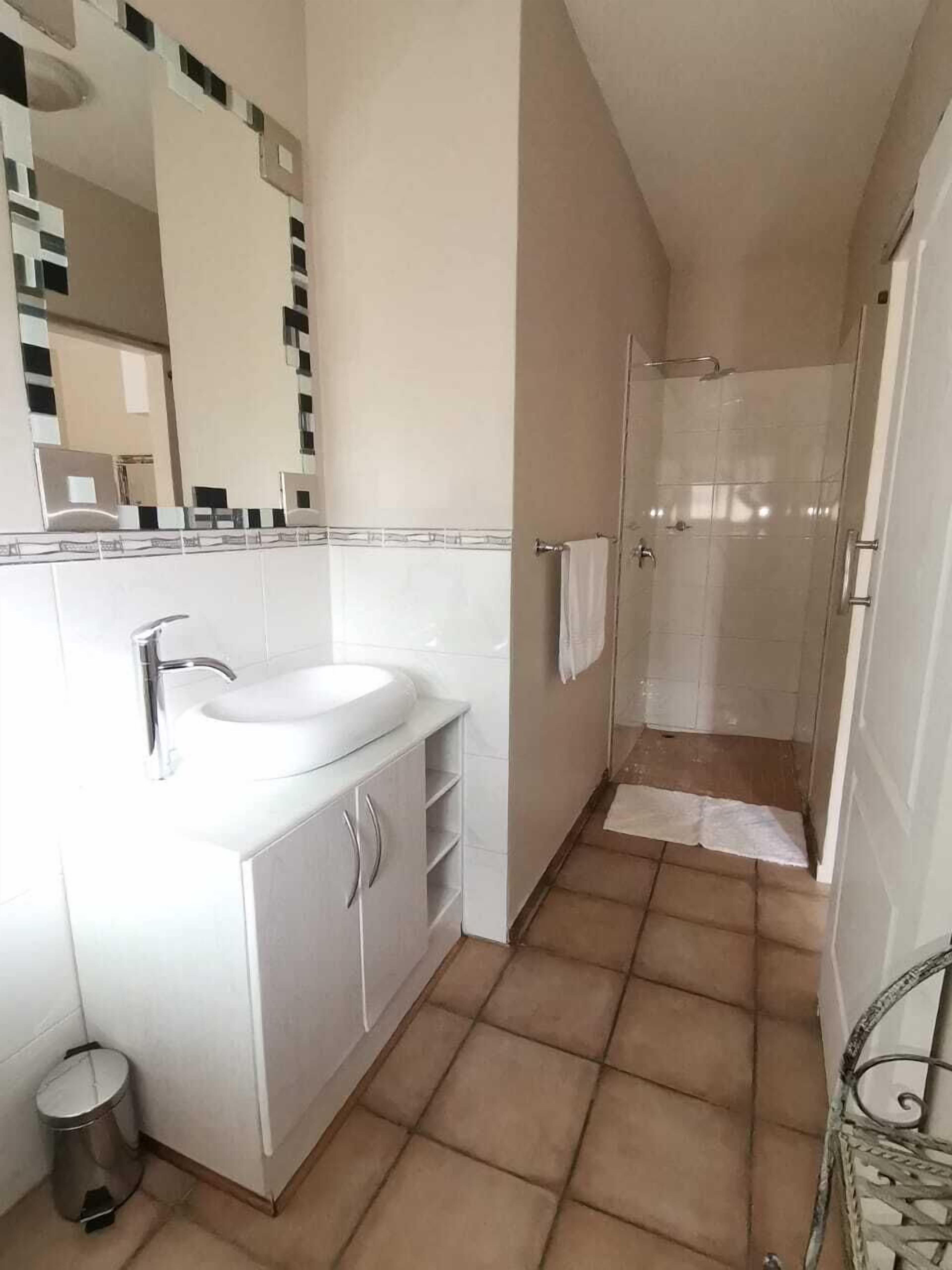Un baño con lavamanos blanco, un espejo y cabina de ducha.