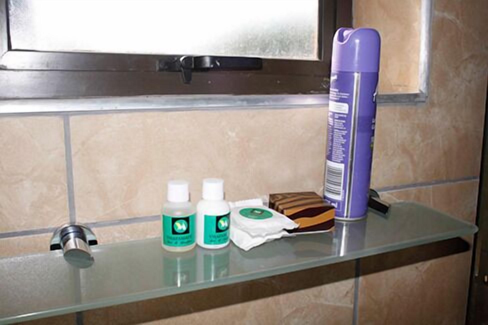 Un estante en el baño con dispensador de jabón, cepillo de dientes, navaja y una botella morada.