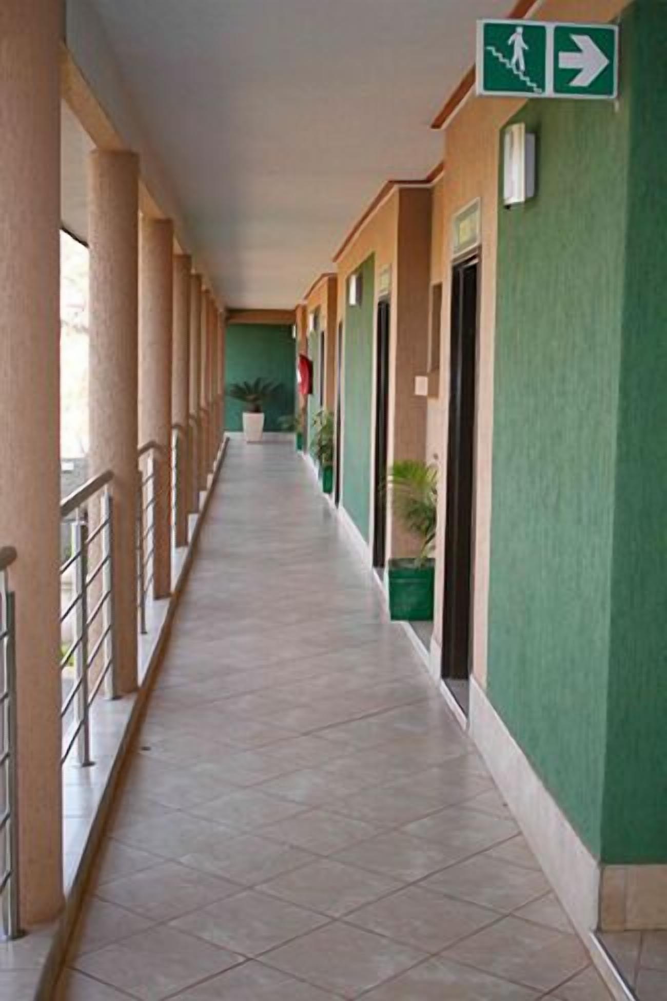 A corridor with a tiled floor, green walls, and a metal railing on one side.