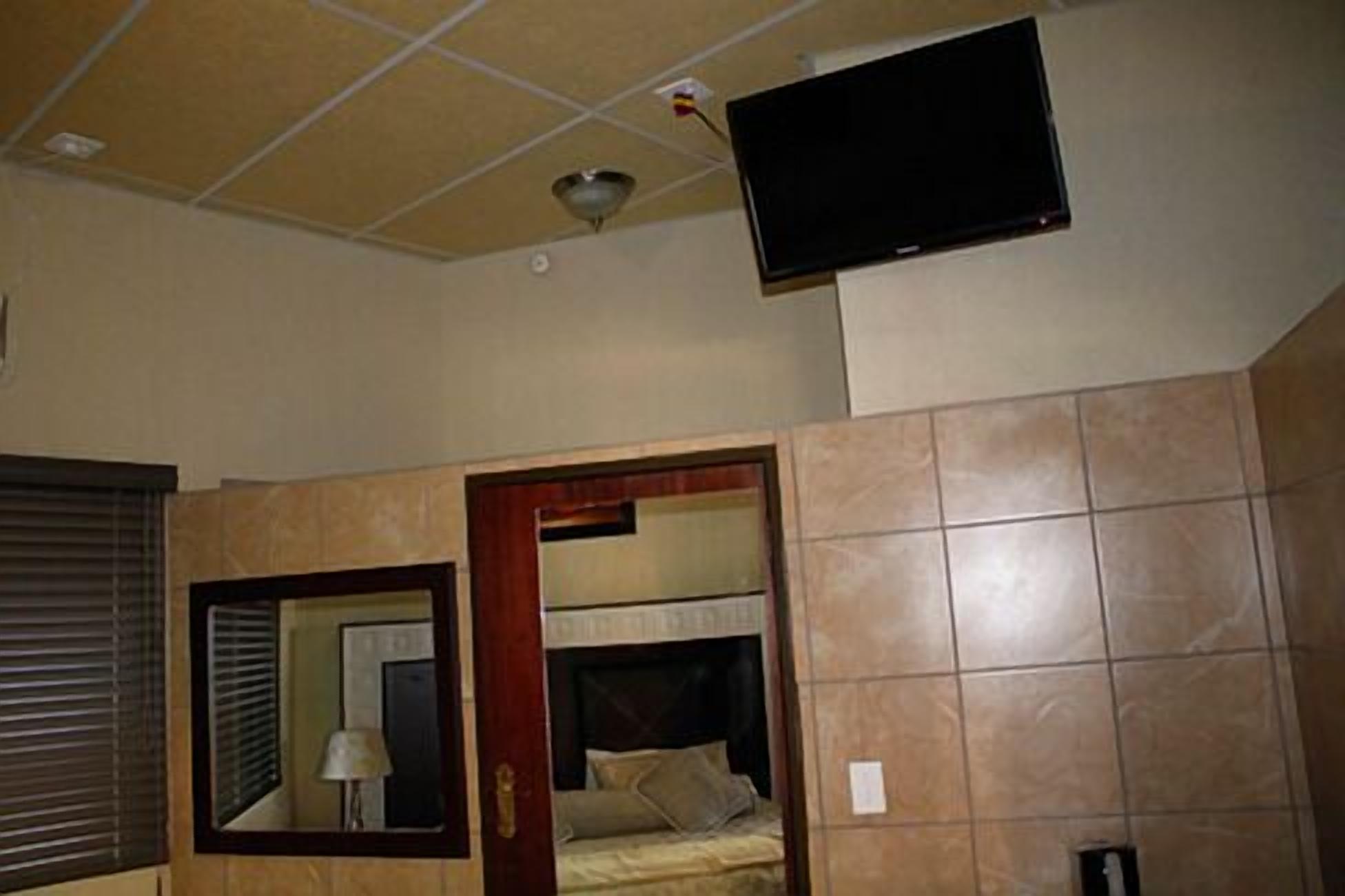 A hotel room with a bed, a television mounted on the wall, a mirror, and a window with blinds.