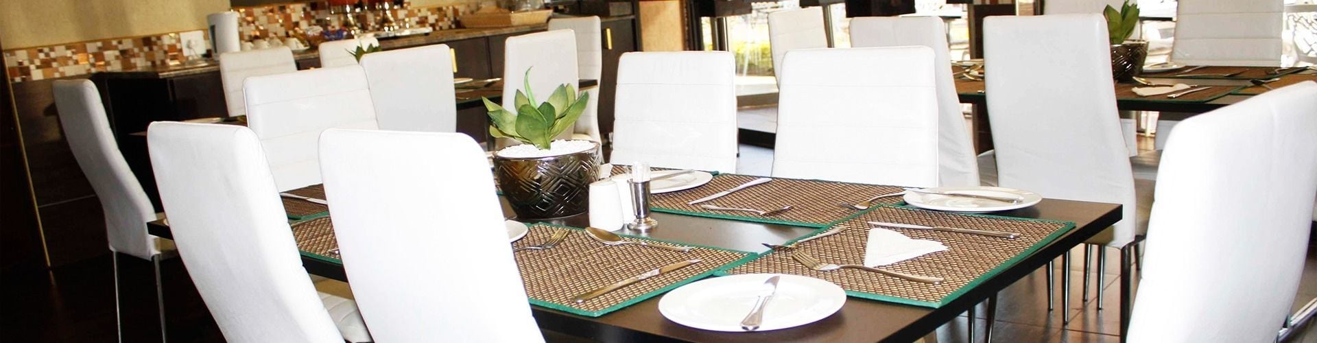 A dining area with white chairs, a table set with plates, cutlery, and a salt and pepper shaker.