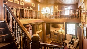 Ein prächtiger Innenraum mit einer Holztreppe, Kristalllüstern und gerahmten Kunstwerken an den Wänden.
