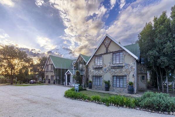A stone building with a green roof, a gravel driveway, and a sign indicating parking availability. - Portland Manor (Knysna)