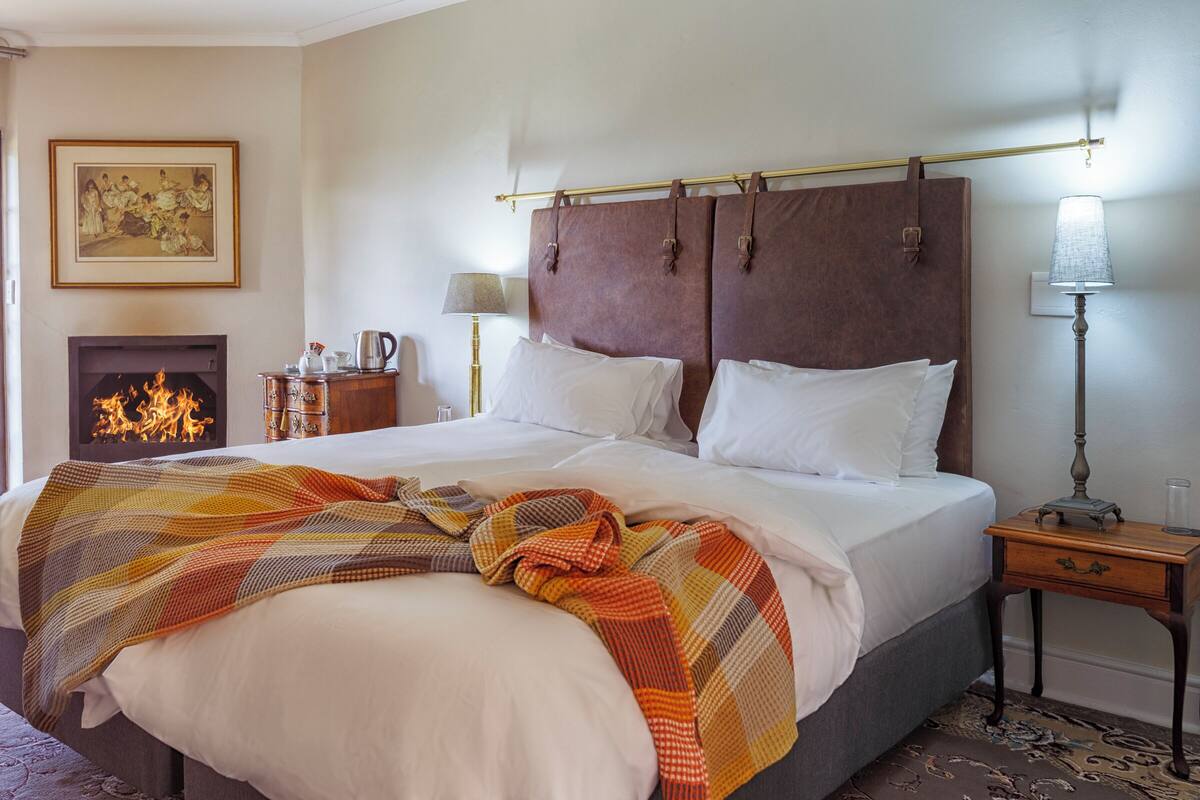 Une chambre d’hôtel avec un grand lit, une cheminée, une table de chevet et une lampe.