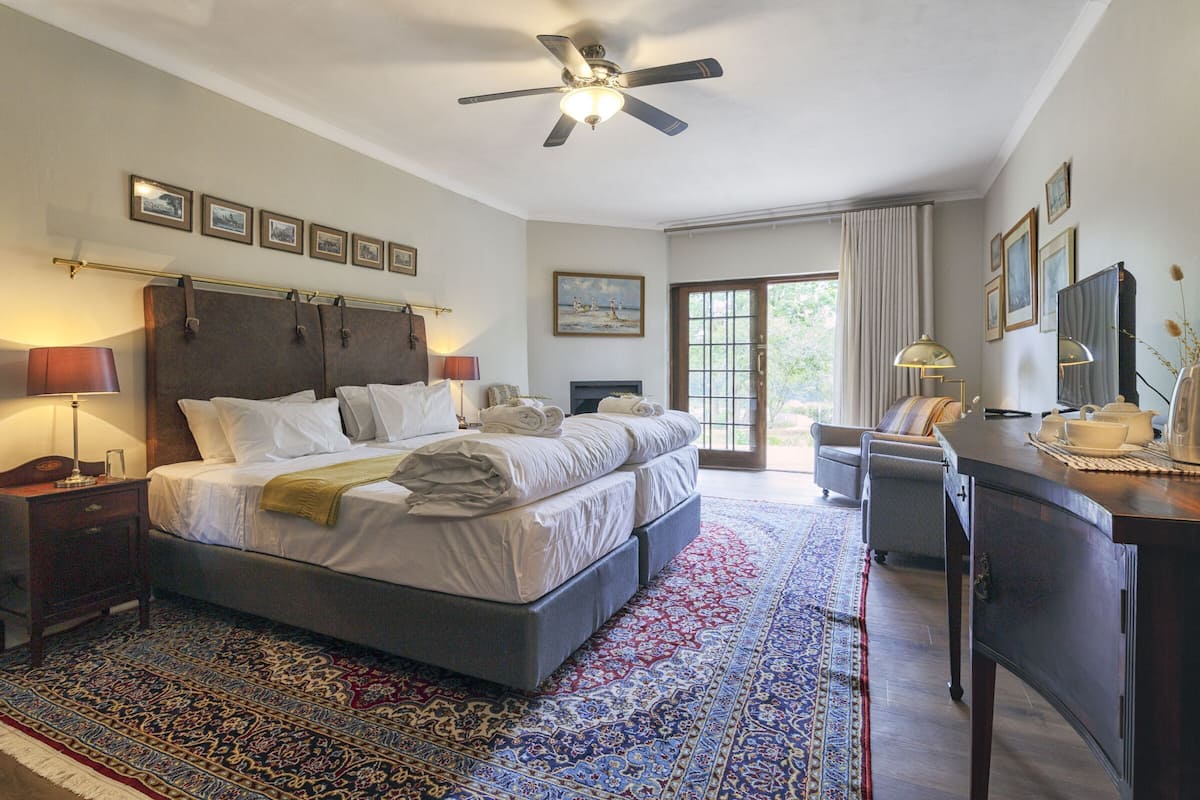 Une chambre d’hôtel avec un grand lit, un bureau, une chaise, un ventilateur de plafond et une vue sur l’extérieur.