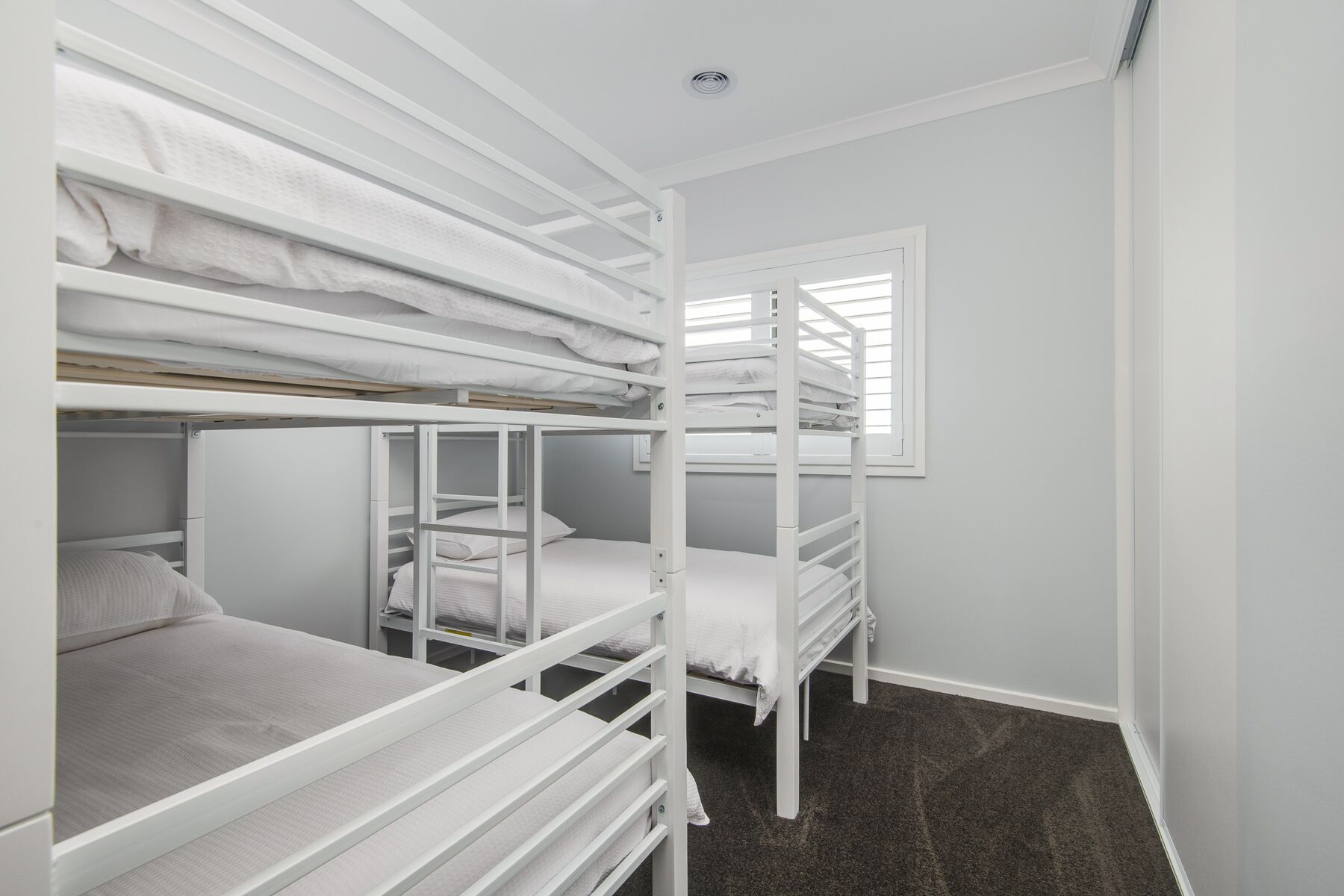A bunk bed room with white bedding and a window.