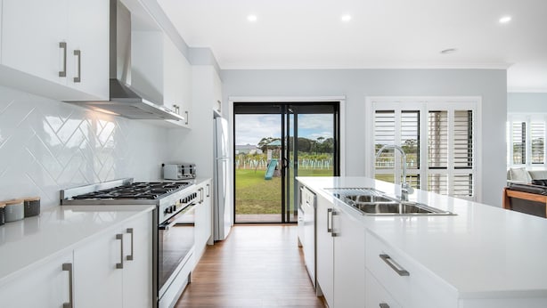 A modern kitchen with white cabinetry, a central island with a sink, and a view of a backyard through a glass door.