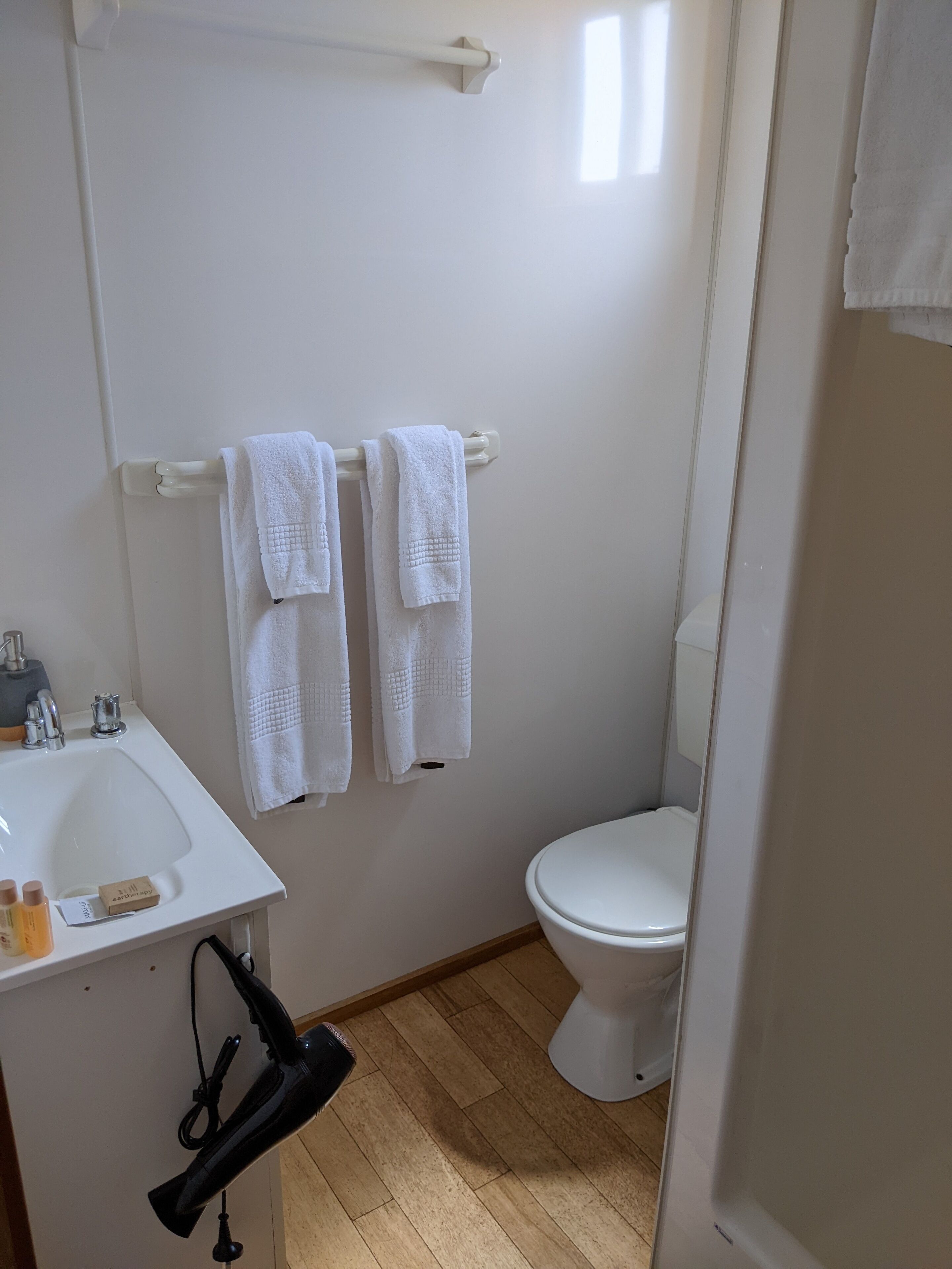 A small, clean bathroom with a white sink, two white towels hanging on a rack, a toilet, and a hairdryer on the floor.