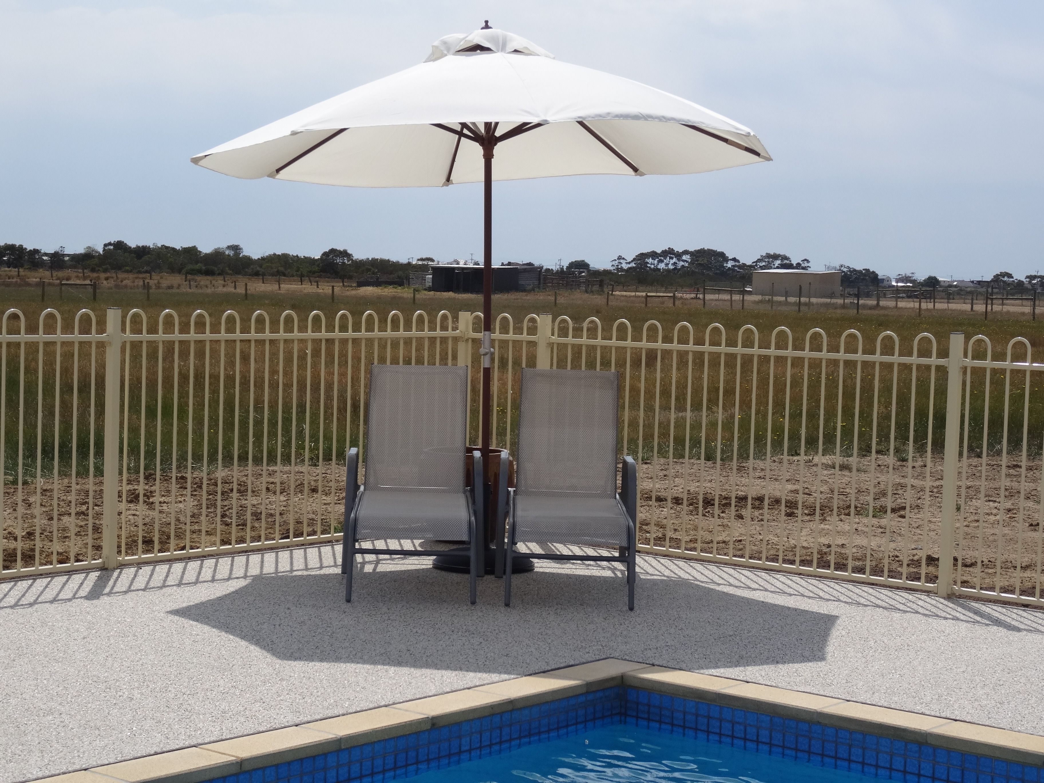 A poolside area with two chairs and a white umbrella.