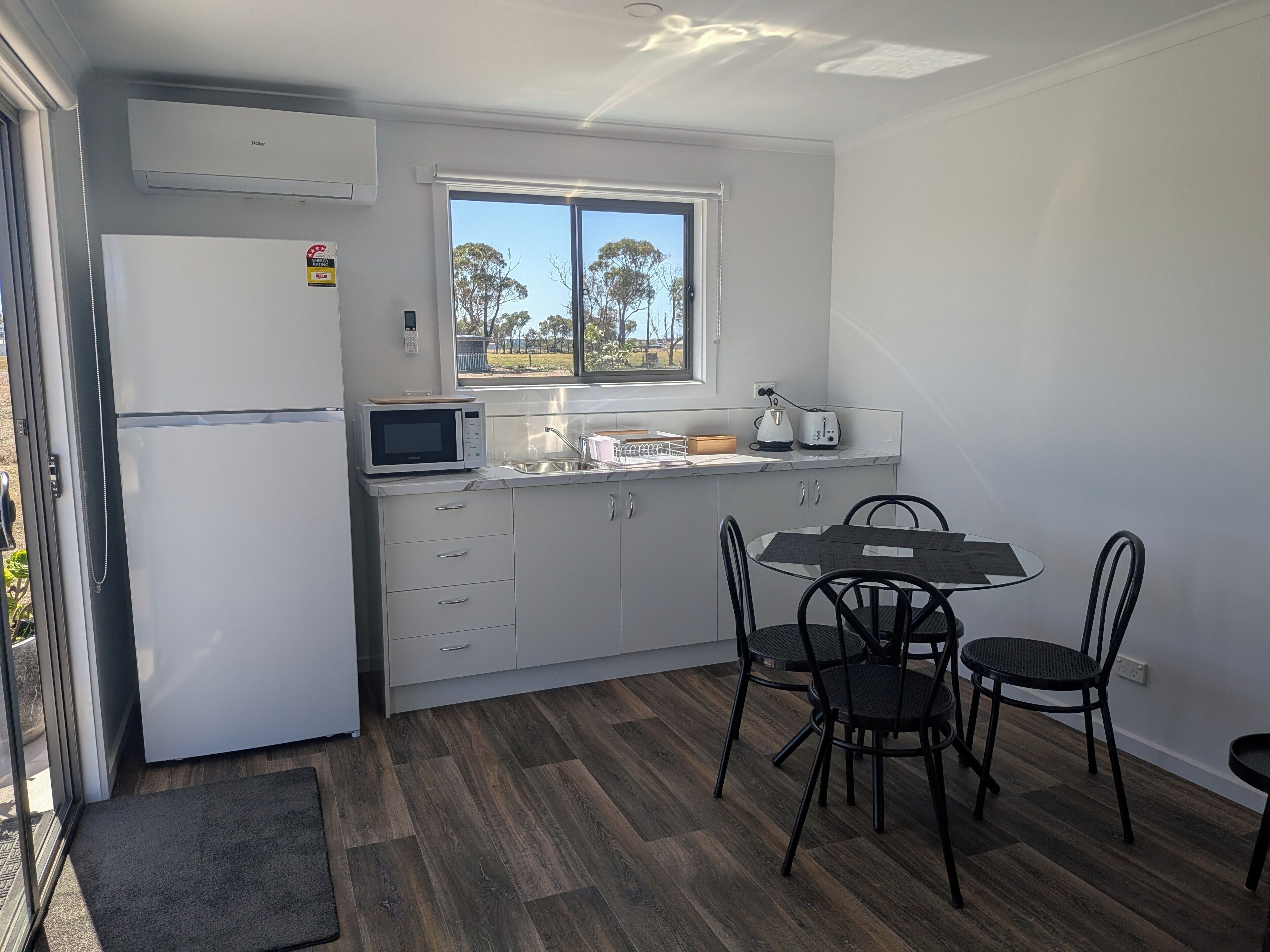 A compact kitchen with a refrigerator, microwave, toaster, and a dining table with chairs.