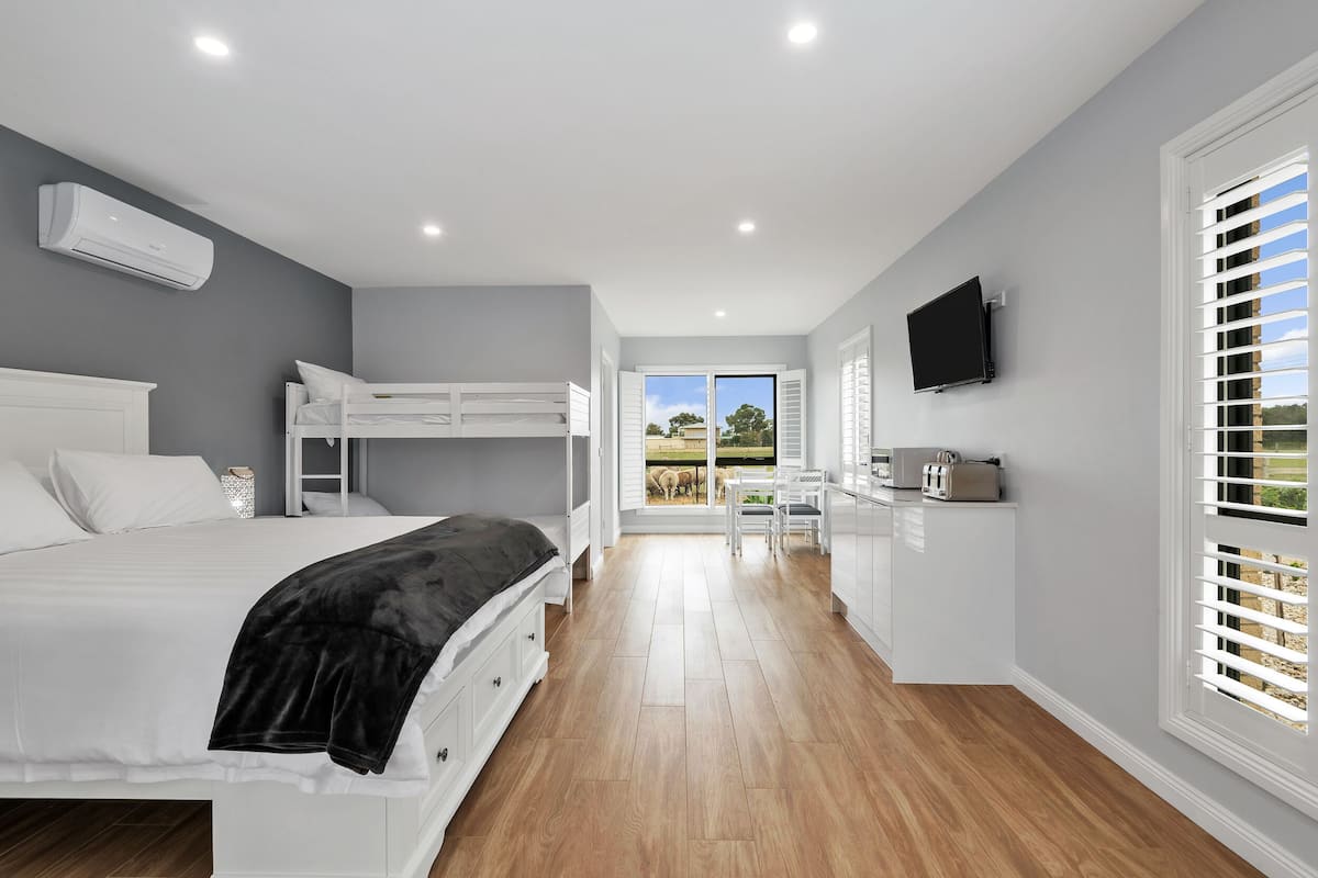 A modern bedroom with a bunk bed, a desk with a chair, and a TV on the wall.