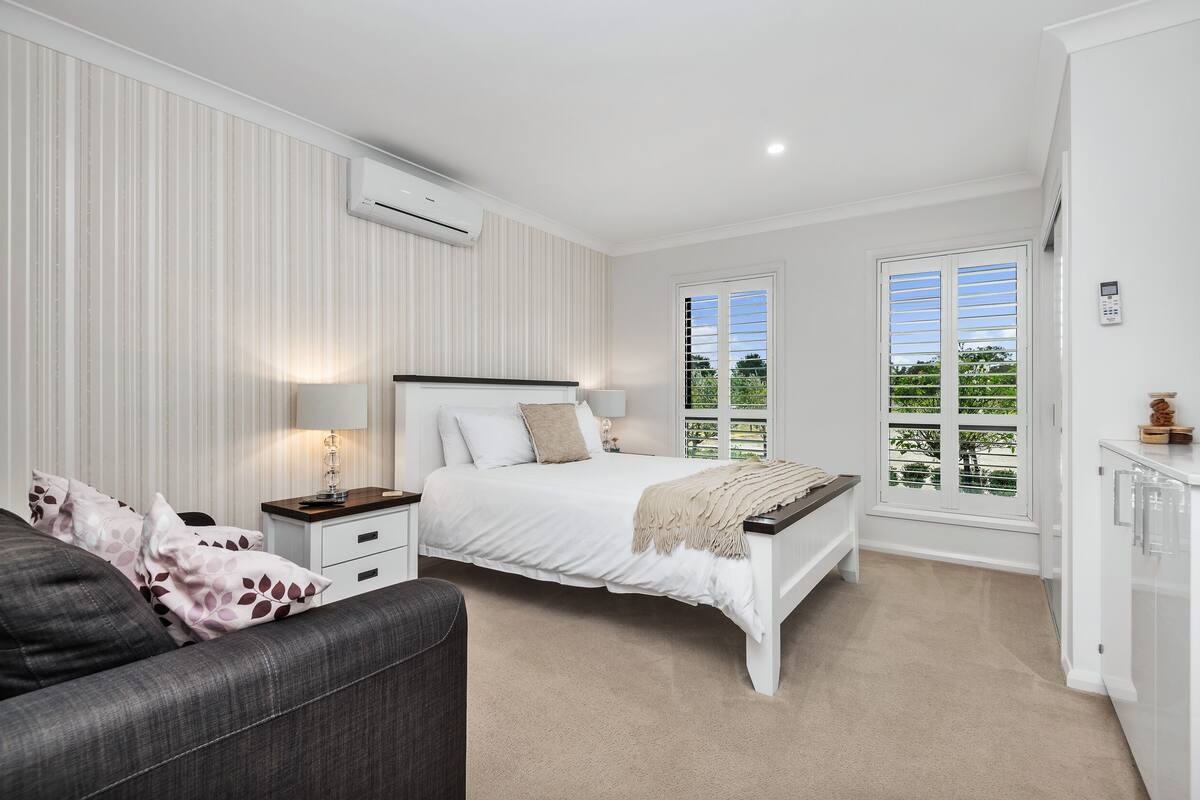 A bedroom with a bed, bedside tables, a lamp, a window, and a view of greenery.