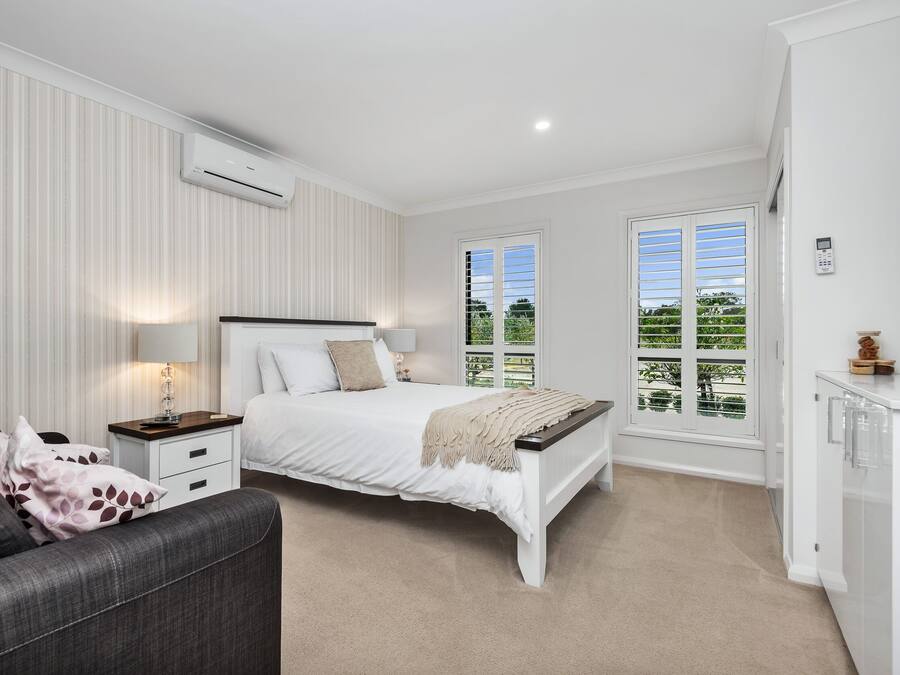 A bedroom with a bed, bedside tables, a lamp, a window, and a view of greenery.