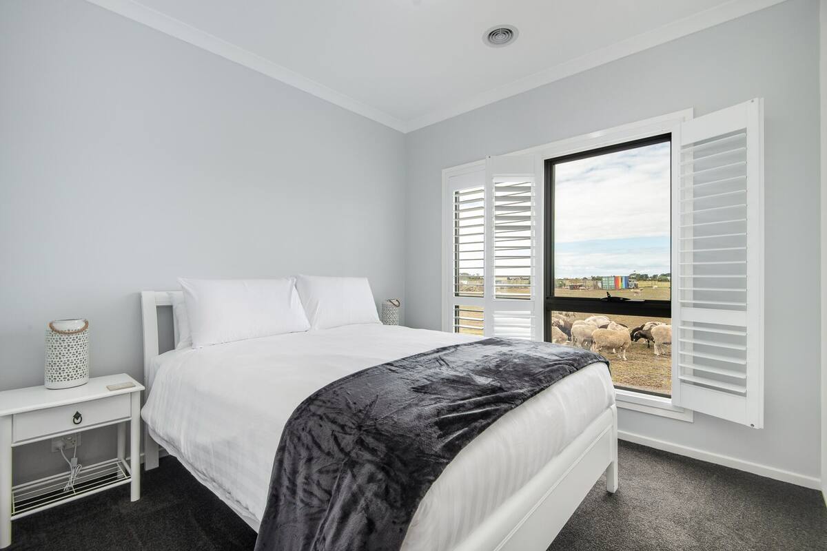 A bedroom with a bed, a nightstand, and a window with shutters.