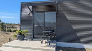 A modern building with a glass door, a small outdoor seating area with metal chairs, and a sign reading "OXLEY LOOSEZ".