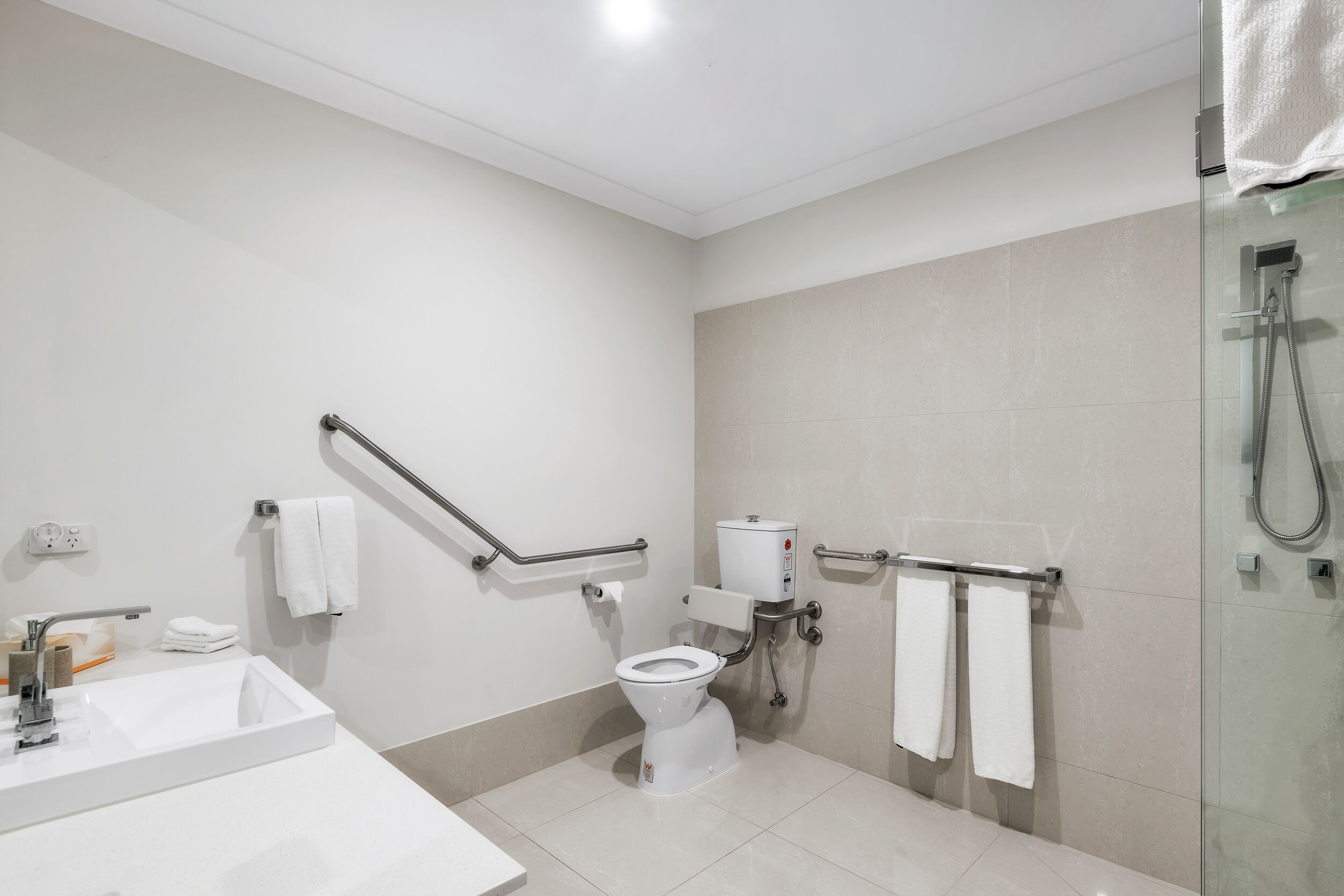 A modern bathroom with a white sink, toilet, and glass shower enclosure.