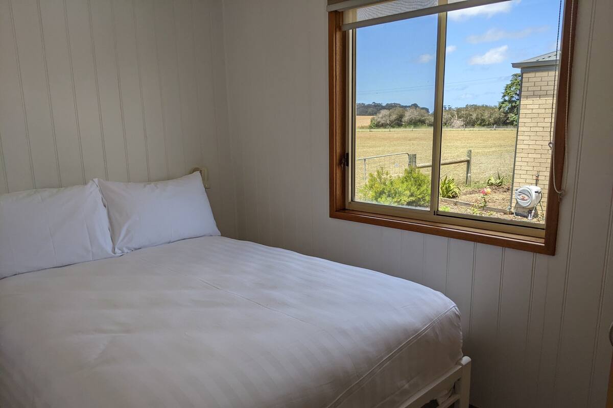 A bedroom with a bed, a window, and a view of a garden and buildings.