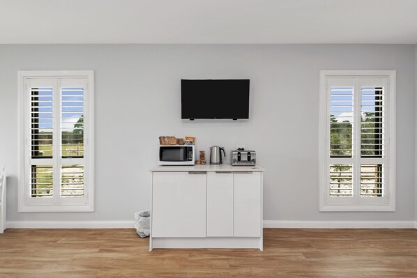 A room with a white cabinet, a flat-screen TV, and two windows with shutters.