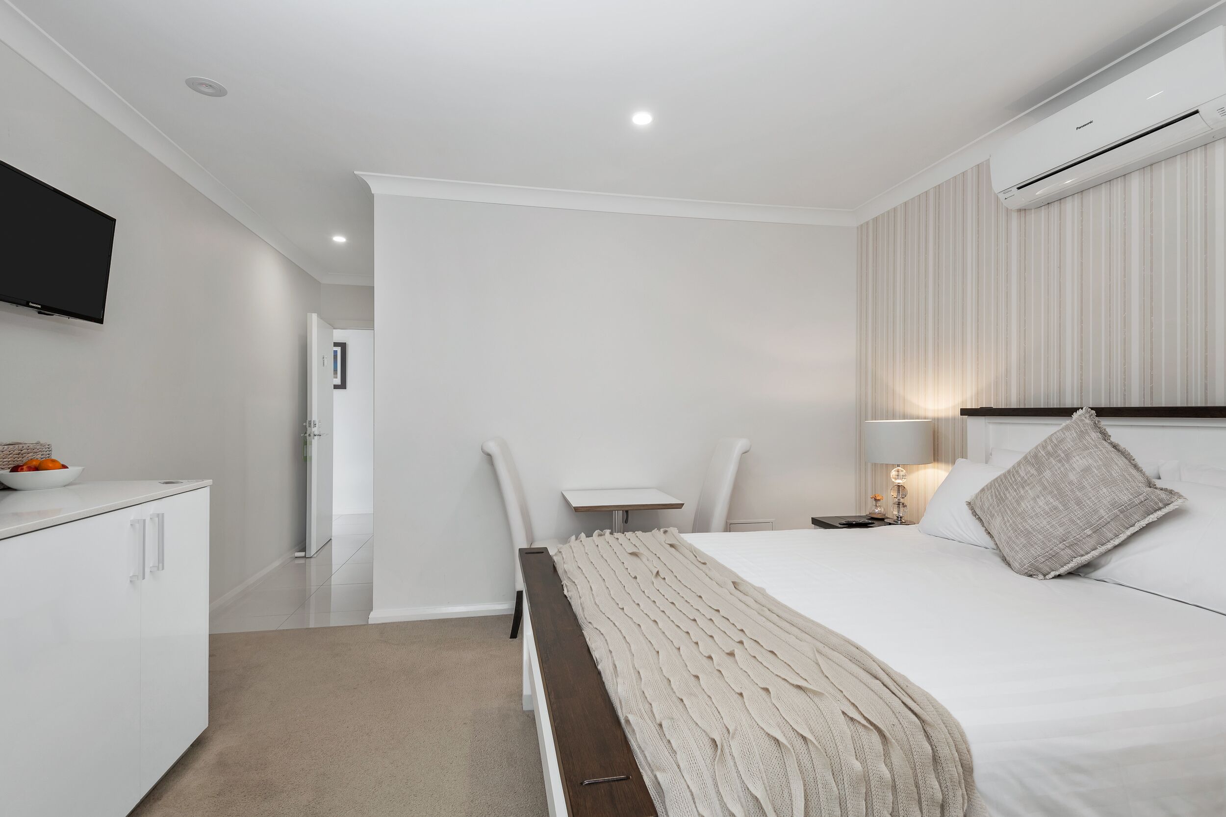 A modern hotel room with a bed, bedside table, lamp, and a flat-screen TV mounted on the wall.