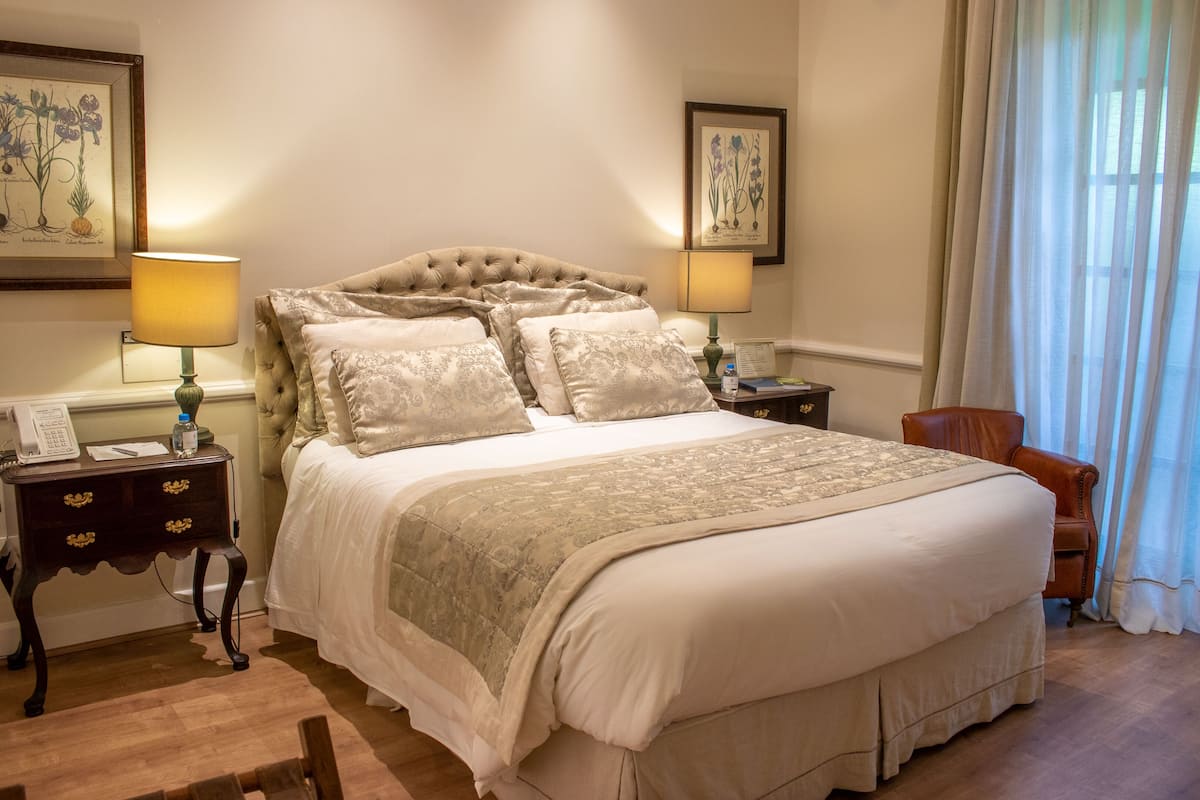A neatly arranged bedroom with a large bed, two bedside tables with lamps, a chair, and framed botanical artwork on the walls.