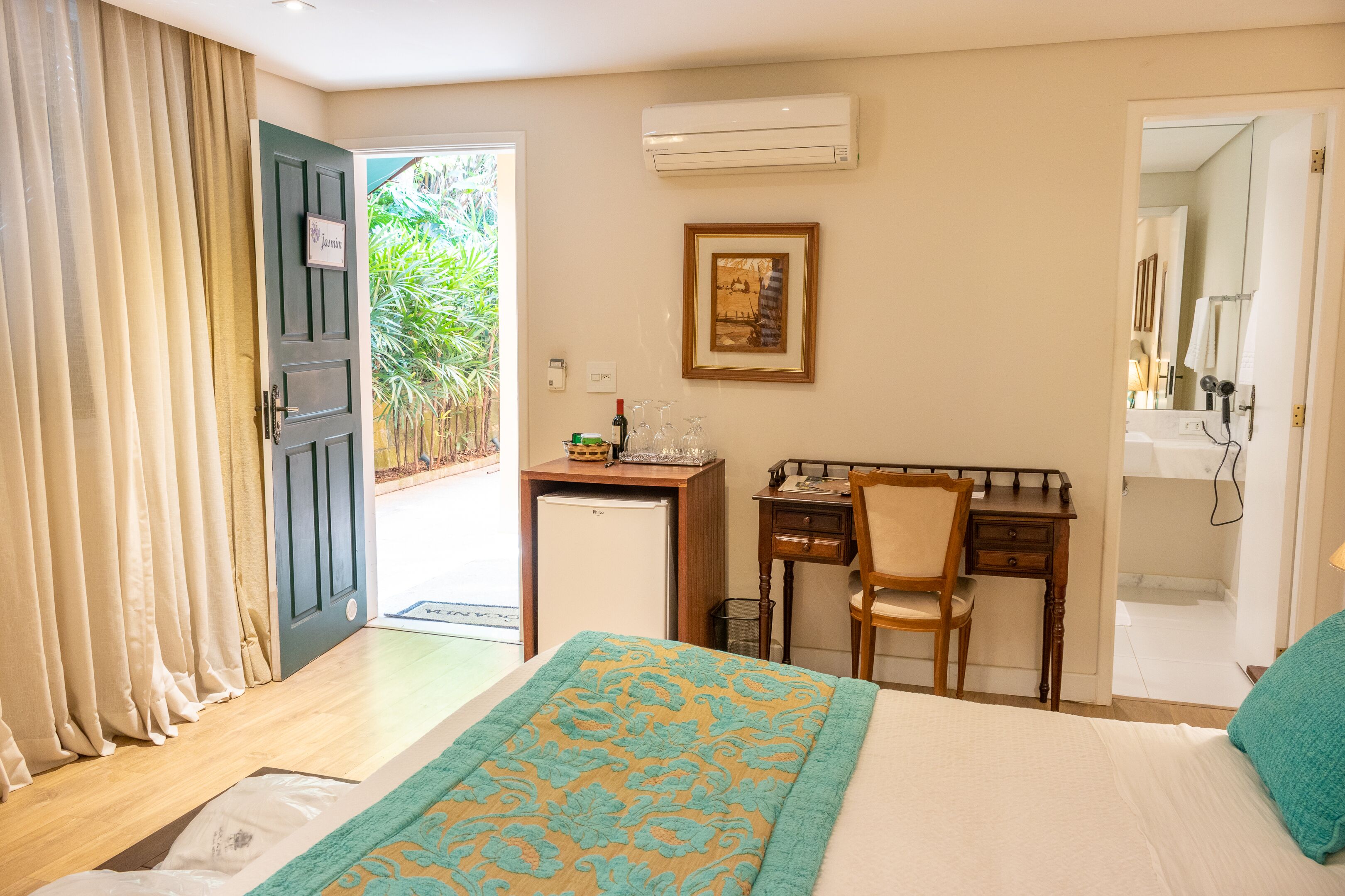 A hotel room with a bed, a desk, a chair, a small refrigerator, and a window with curtains.