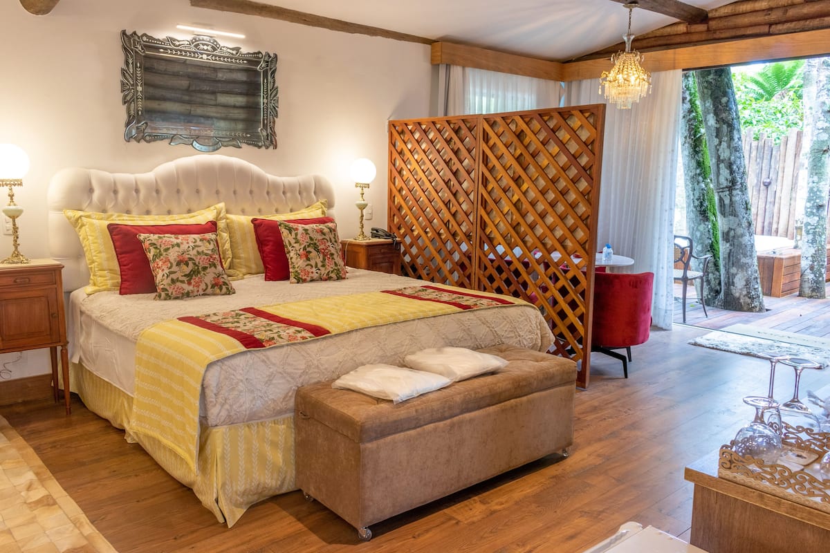A bedroom with a large bed, wooden floor, and a view of the outdoors.