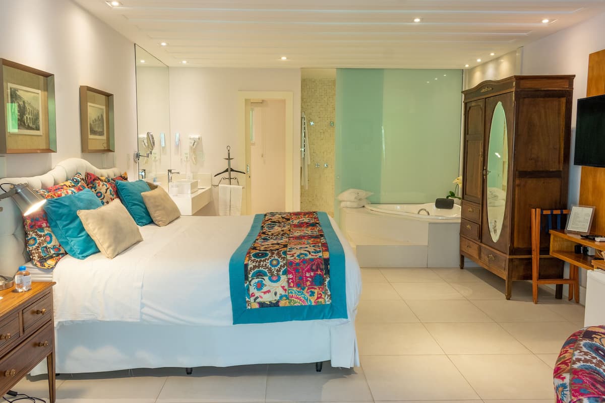 A bedroom with a large bed, a wooden wardrobe, a desk with a chair, and a bathroom with a bathtub.