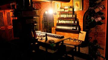 Um quarto com pouca luz, com uma mesa de madeira, cadeiras e uma estante cheia de garrafas de vinho.