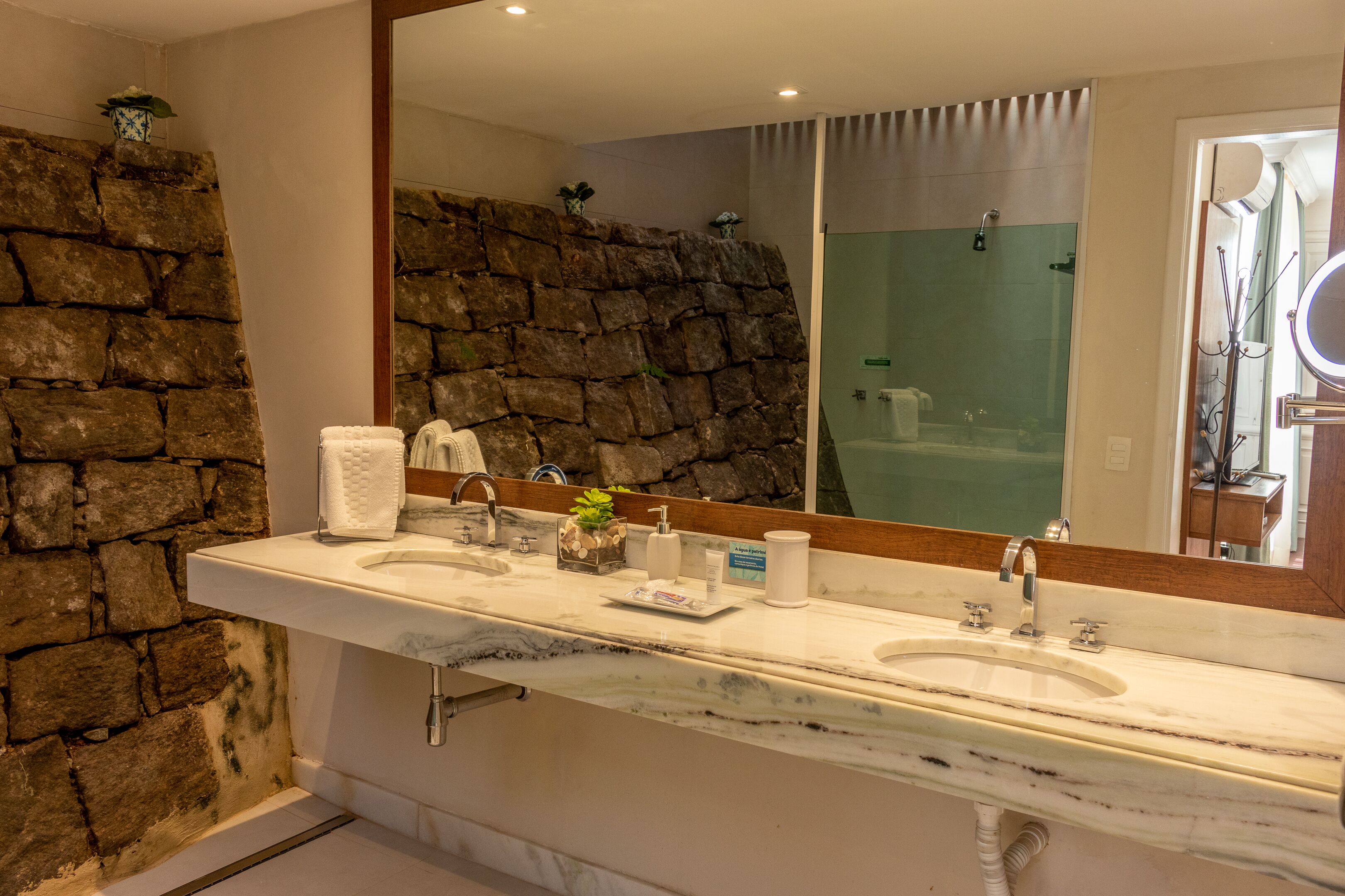 A bathroom with a stone wall, a marble sink, a large mirror, and a shower area.