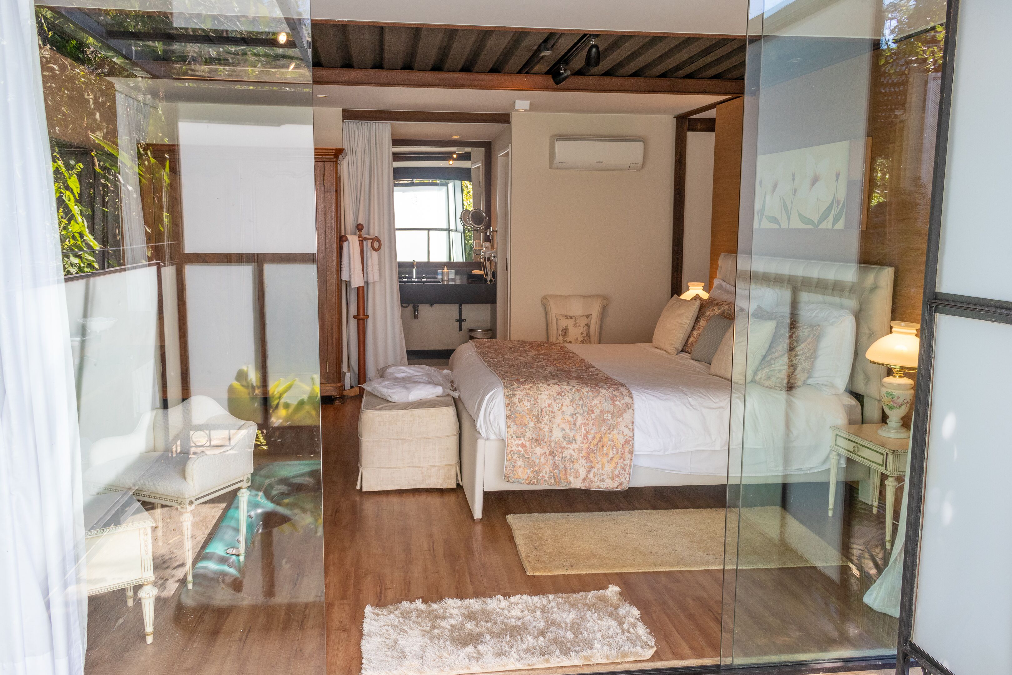 A modern bedroom with a large bed, a small bedside table, a chair, and a mirror.