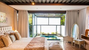 A spacious bedroom with a large bed, a sitting area, a vanity with a mirror, and a view of a swimming pool. - Locanda Della Mimosa (Petrópolis)